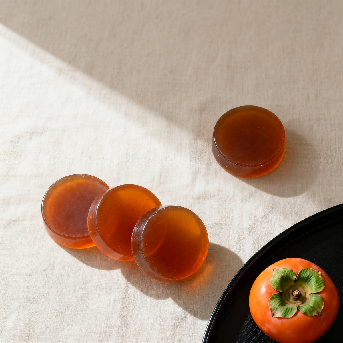 Four Yuagari persimmon soap bars on linen beside a persimmon on a lacquer tray